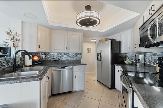 kitchen with appliances with stainless steel finishes, sink, light tile patterned floors, and a tray ceiling