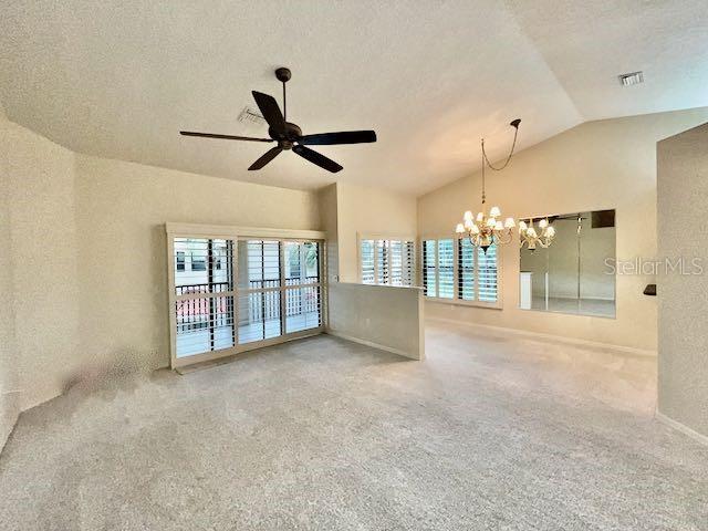 empty room featuring a textured ceiling, carpet flooring, lofted ceiling, and ceiling fan with notable chandelier