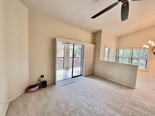 carpeted empty room featuring vaulted ceiling and ceiling fan with notable chandelier