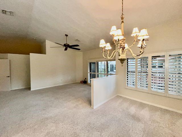 spare room with carpet, vaulted ceiling, and ceiling fan with notable chandelier