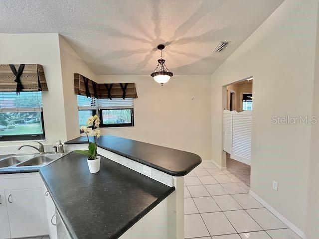 kitchen featuring light tile patterned floors, a textured ceiling, pendant lighting, white cabinets, and sink