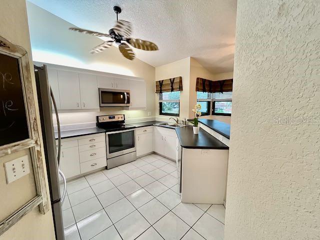 kitchen featuring lofted ceiling, ceiling fan, sink, appliances with stainless steel finishes, and white cabinets