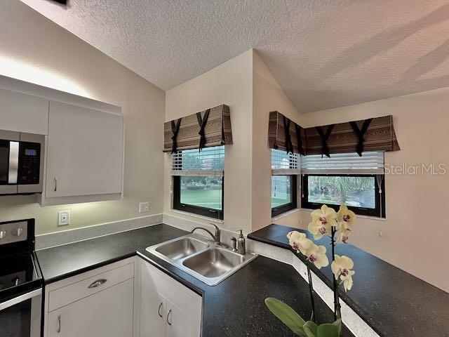 kitchen with white cabinetry, appliances with stainless steel finishes, lofted ceiling, a textured ceiling, and sink