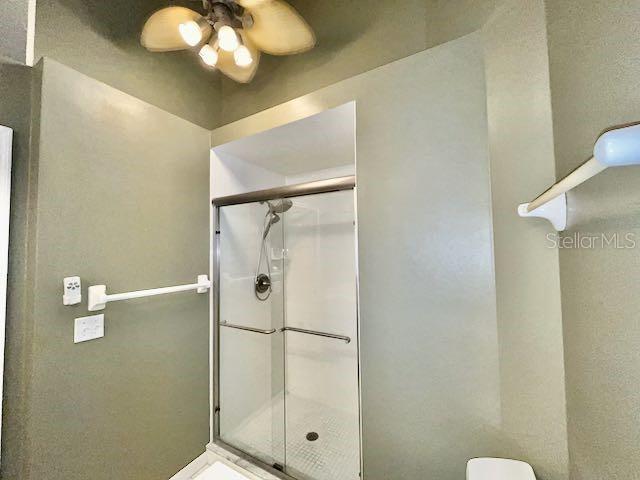 bathroom with ceiling fan, toilet, and a shower with door