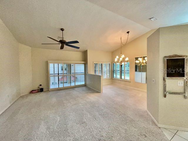 carpeted empty room with a textured ceiling, lofted ceiling, and ceiling fan with notable chandelier