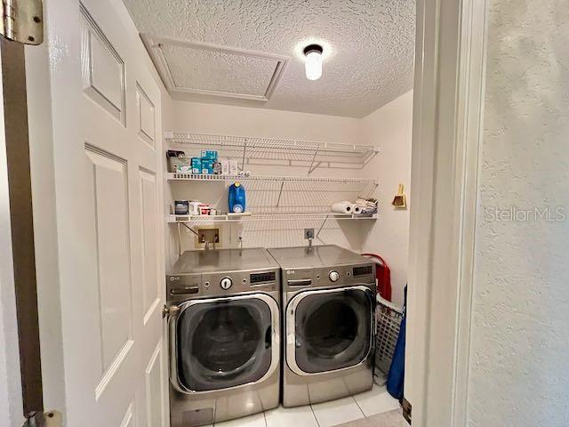 washroom with washing machine and dryer, light tile patterned flooring, and a textured ceiling