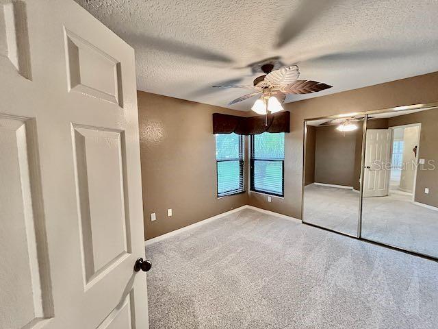 unfurnished bedroom featuring ceiling fan, a textured ceiling, a closet, and carpet flooring