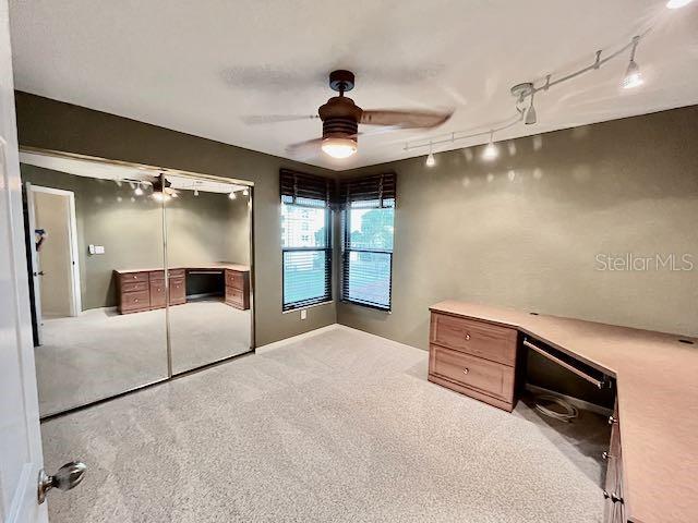 unfurnished bedroom featuring ceiling fan, rail lighting, light colored carpet, and a closet