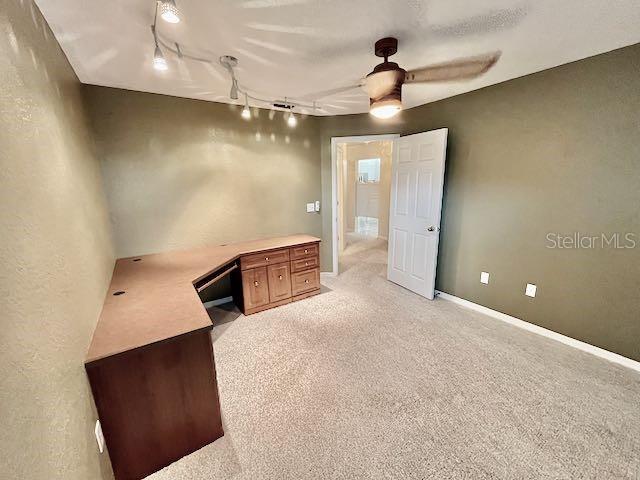 unfurnished office with ceiling fan, light colored carpet, and track lighting