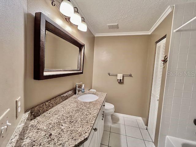 full bathroom featuring a textured ceiling, toilet, ornamental molding, and tile patterned floors