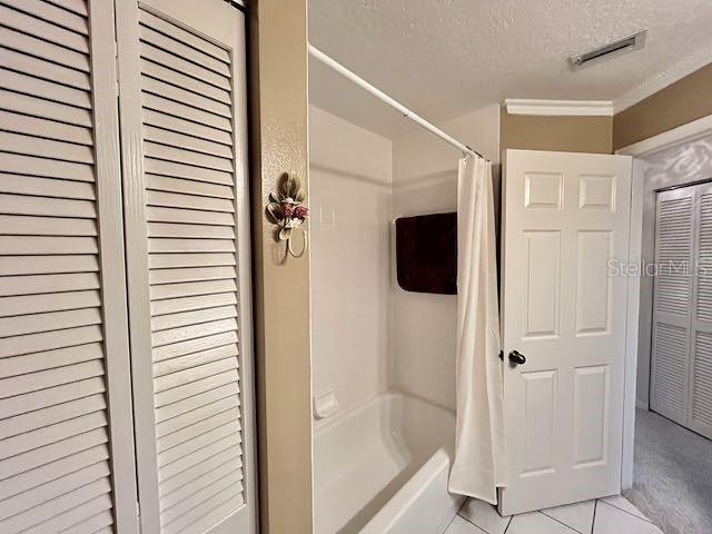 bathroom featuring a textured ceiling, crown molding, tile patterned floors, and shower / bath combo with shower curtain