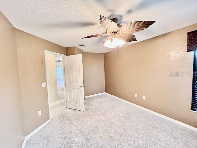 unfurnished bedroom with ceiling fan, light colored carpet, and a textured ceiling