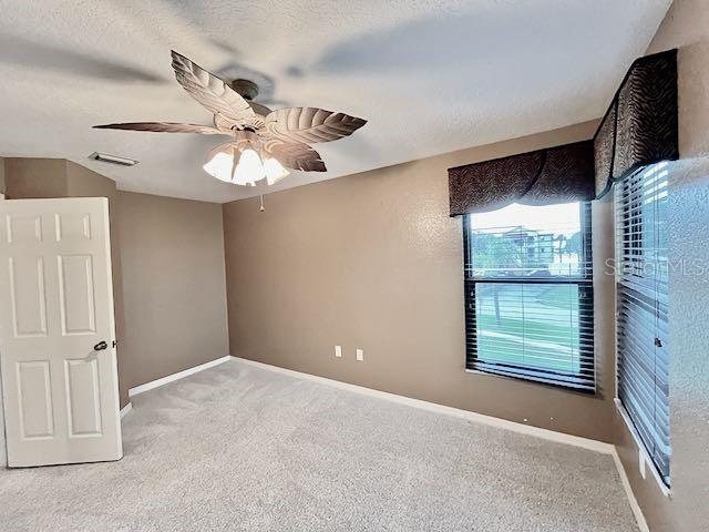 carpeted spare room featuring ceiling fan and a textured ceiling