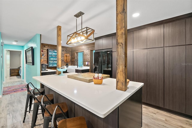 kitchen featuring pendant lighting, black refrigerator with ice dispenser, wooden walls, a kitchen breakfast bar, and light wood-type flooring