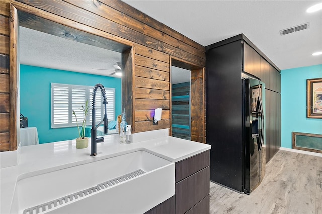 kitchen featuring a textured ceiling, sink, light hardwood / wood-style flooring, ceiling fan, and wood walls