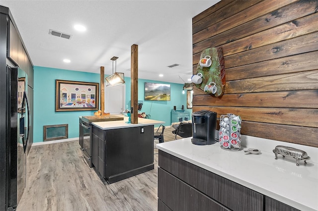 kitchen with a textured ceiling, black appliances, a kitchen island, decorative light fixtures, and light wood-type flooring