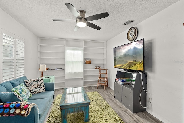 living room with ceiling fan, a textured ceiling, and light wood-type flooring