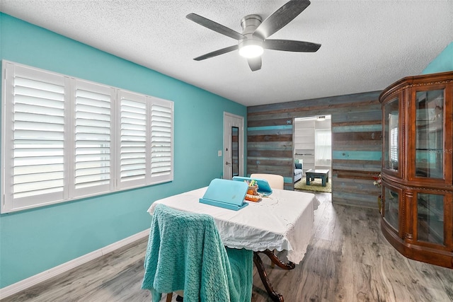 dining room with ceiling fan, wood walls, plenty of natural light, and wood-type flooring