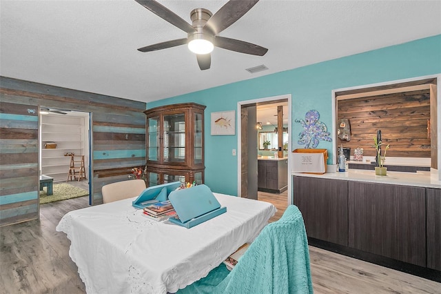 dining room with light wood-type flooring, ceiling fan, wooden walls, and a textured ceiling