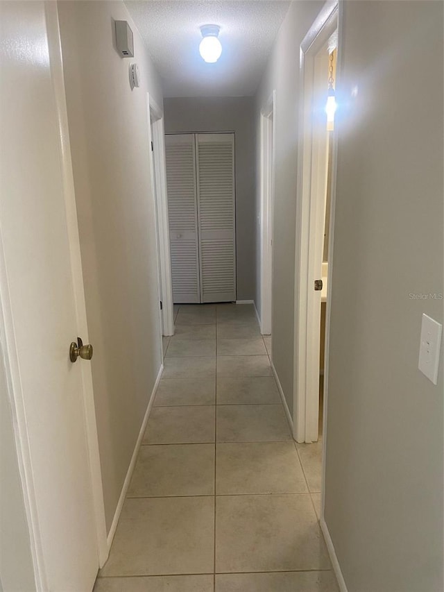 corridor with a textured ceiling and light tile patterned flooring