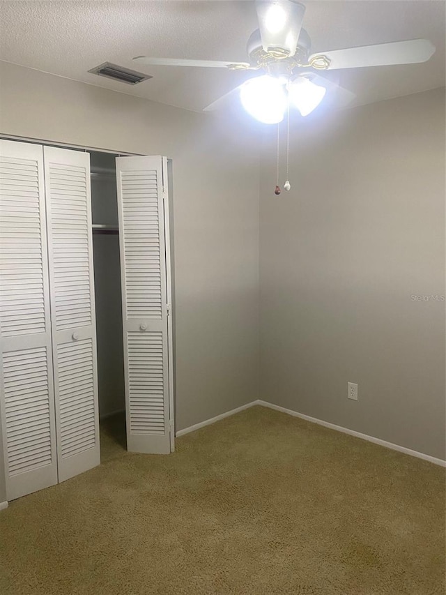 unfurnished bedroom with a textured ceiling, ceiling fan, carpet flooring, and a closet