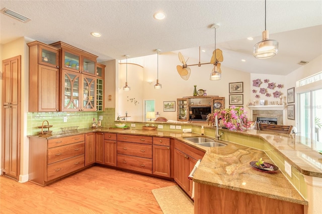 kitchen featuring decorative light fixtures, vaulted ceiling, light hardwood / wood-style floors, sink, and a textured ceiling