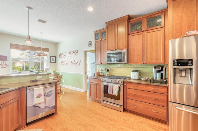 kitchen featuring light hardwood / wood-style floors, stainless steel appliances, backsplash, a textured ceiling, and pendant lighting