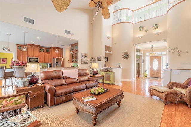 living room with light wood-type flooring, ceiling fan, and a high ceiling