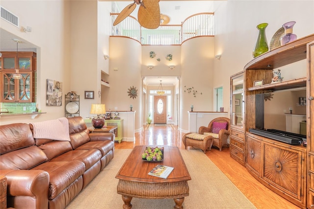 living room with ceiling fan, light wood-type flooring, and a towering ceiling