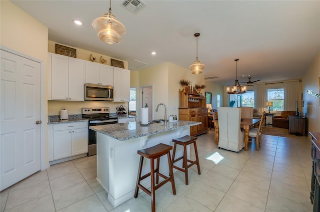 kitchen with appliances with stainless steel finishes, decorative light fixtures, white cabinetry, dark stone counters, and a center island with sink