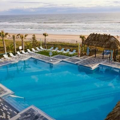 community pool featuring a water view, fence, a view of the beach, and a patio