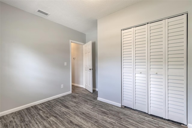 unfurnished bedroom featuring a textured ceiling, dark hardwood / wood-style floors, and a closet