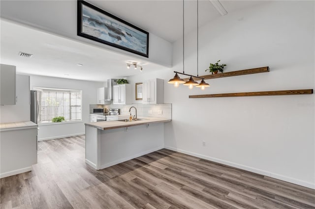 kitchen featuring decorative light fixtures, tasteful backsplash, a kitchen bar, kitchen peninsula, and light hardwood / wood-style flooring