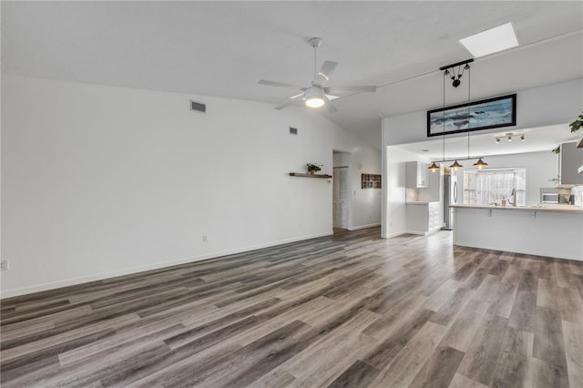 unfurnished living room with wood-type flooring, vaulted ceiling with skylight, and ceiling fan