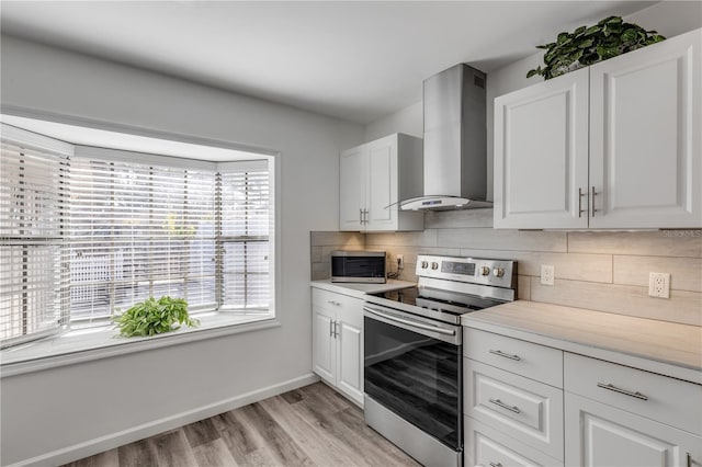 kitchen featuring wall chimney exhaust hood, white cabinetry, a healthy amount of sunlight, stainless steel appliances, and decorative backsplash