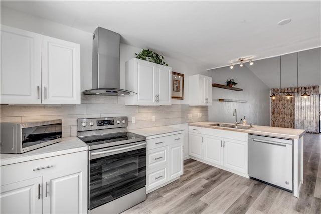 kitchen with pendant lighting, wall chimney range hood, sink, white cabinetry, and stainless steel appliances