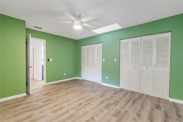 unfurnished bedroom with multiple closets, ceiling fan, a skylight, and light hardwood / wood-style floors