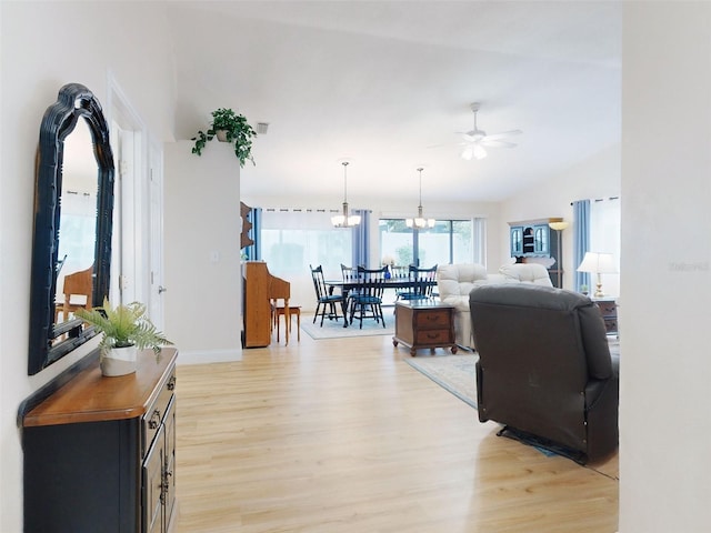 living room with lofted ceiling, ceiling fan with notable chandelier, and light wood-type flooring