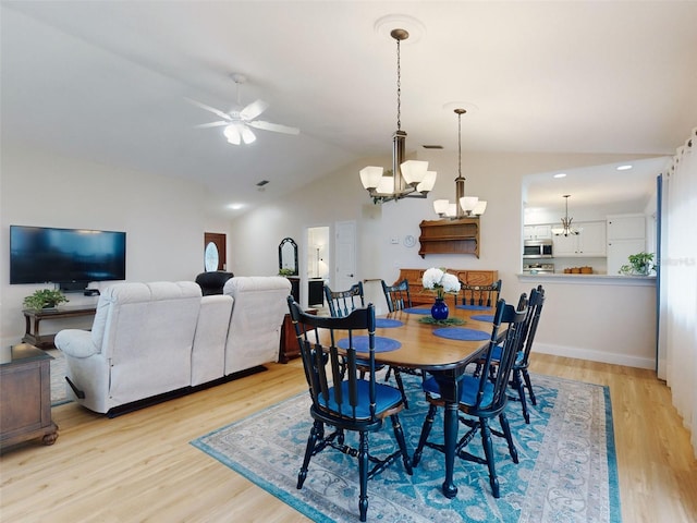 dining room with ceiling fan with notable chandelier, light hardwood / wood-style flooring, and vaulted ceiling