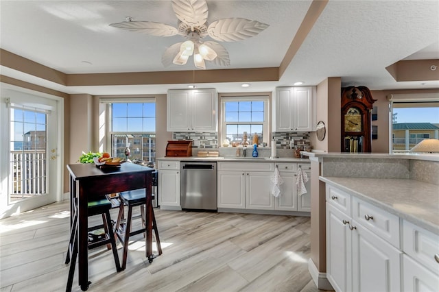 kitchen with sink, white cabinets, backsplash, stainless steel dishwasher, and light hardwood / wood-style flooring