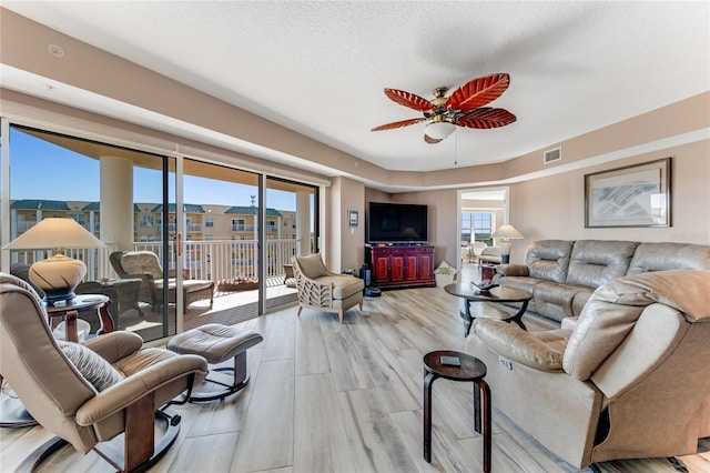 living room with a textured ceiling, light hardwood / wood-style flooring, and ceiling fan