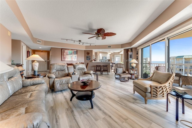 living room with a textured ceiling, rail lighting, ceiling fan, and light wood-type flooring