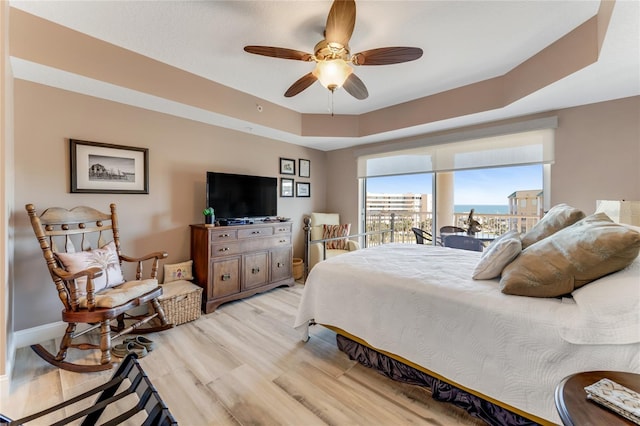 bedroom featuring a raised ceiling, light wood-type flooring, and ceiling fan