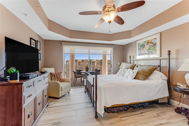 bedroom featuring ceiling fan, a tray ceiling, and light wood-type flooring