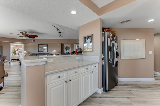 kitchen featuring white cabinetry, kitchen peninsula, stainless steel refrigerator with ice dispenser, light stone countertops, and a textured ceiling