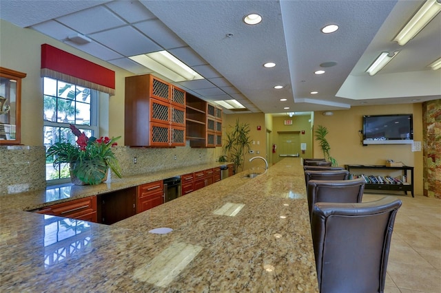 kitchen with sink, light stone counters, tasteful backsplash, light tile patterned flooring, and kitchen peninsula