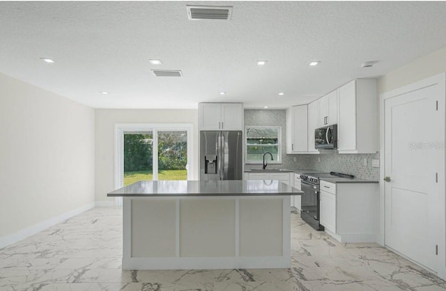 kitchen featuring appliances with stainless steel finishes, white cabinetry, backsplash, a center island, and a textured ceiling