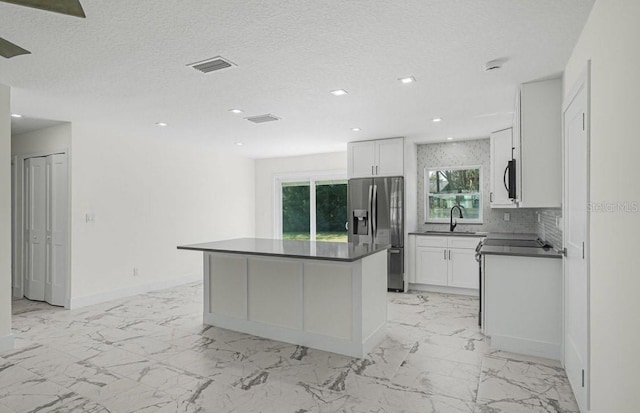 kitchen featuring white cabinetry, tasteful backsplash, a textured ceiling, a kitchen island, and stainless steel appliances