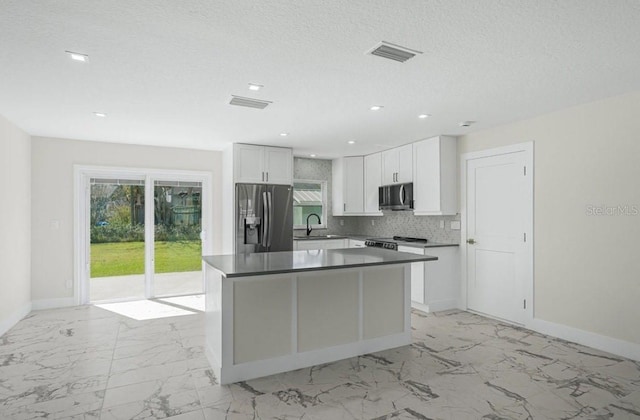 kitchen with appliances with stainless steel finishes, sink, white cabinets, decorative backsplash, and a center island