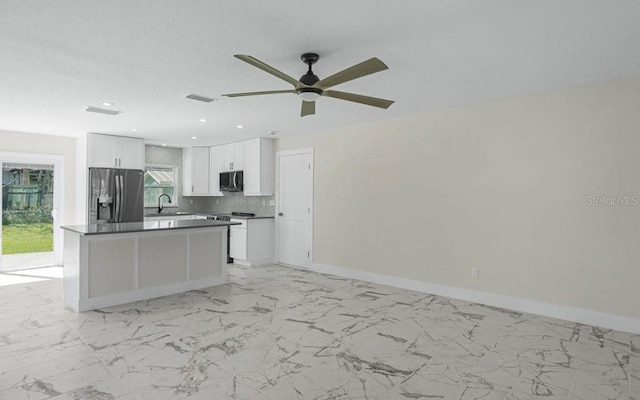 kitchen with stainless steel fridge with ice dispenser, a kitchen island, white cabinets, ceiling fan, and backsplash